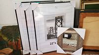 Three white wall frames still in packaging with protective corners, stacked together showing size 22x28 inches.