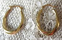 Pair of oval twisted design 10K yellow gold hoop earrings laid flat on a lace fabric background, showing front view and lighting highlight on gold polish