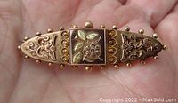 Top view of the antique two-tone floral pin showing the detailed embossed and beaded design with green gold leaves in the center square and cannonball border beads along the edges.