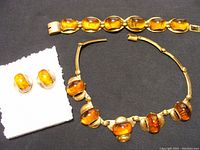 Full set showing amber necklace, bracelet, and earrings laid on black background with white cloth underneath earrings.