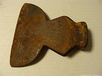 Front view of the rusty axe or hatchet head showing its wide blade and thick poll.