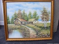 Full view of the framed country scene oil painting, showing the rural landscape with two wooden buildings, pond, dirt path, and trees.