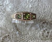 Front view of sterling silver ring showing three round peridot stones and decorative milgrain and engraving.