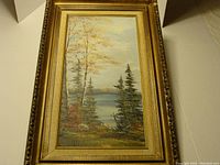 Full view of framed oil painting depicting lake and trees in autumn colors.