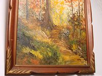 Front angled view of the oil painting showing forest landscape with autumn colors and the carved wooden frame.