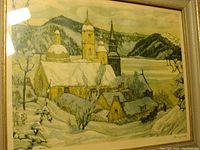 Framed art print showing a snowy winter village with church steeples and mountainous background.