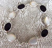Bracelet laid out on lace fabric showing arrangement of black onyx and mother of pearl stones set in sterling silver bezels.