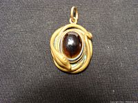 Front view of the antique pendant showing the dark oval stone surrounded by the winding snake brass setting with visible green patina.