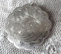 Top view showing scalloped edges and detailed flower and leaf engravings on the sterling silver surface of the brooch.