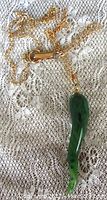 Full length image of gold tone chain with green jade pepper pendant resting on lace fabric.