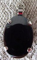 Close up front view of oval hematite stone set in sterling silver prong setting on lace background.