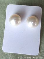 Front view of two round creamy white cultured pearl stud earrings on a white display card