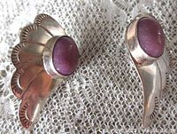 Close-up image showing the front side of the two stamped sterling silver earrings with lavender jade cabochons set in engraved scalloped edges.