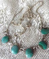 Top view showing the front of the necklace with five oval turquoise stones evenly spaced on a sterling silver box link chain, laying on lace fabric.