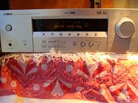 Full front view showing silver metal front panel of AV receiver with lit digital display and front controls.