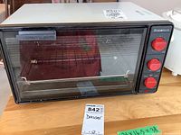 Beaumark toaster oven front view showing glass door, three red control knobs, and interior rack on wooden surface.