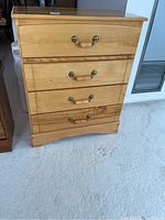 Front view of the light wood dresser with four drawers, showing metal and wood handles and visible condition of the wood surfaces.