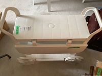 White plastic exterior bar cart with two tiers, grid textured top, and two handles. The wheels are wide and flat for easy movement. The top tier is retracted to 12 inches deep in this view.