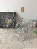 Photo showing crystal platter, lidded bowls, decanter, pitcher arranged on table in front of box