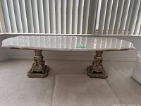 Front view of long rectangular marble coffee table with two ornate metal pedestal legs and beveled edges.
