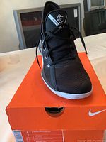 Front view of black Nike Zoom Evidence 111 shoe on orange Nike box, showing mesh upper, laces and partial swoosh logo.