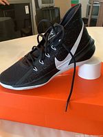 Side view of black Nike Zoom Evidence 111 shoe showing white swoosh and midsoles on an orange box.