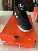 Right side view of black Nike Zoom athletic shoe with white swoosh and red heel accent on orange Nike box