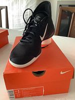 Black Nike Zoom men's athletic shoe on orange Nike shoe box, size label visible on box.