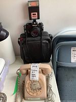 Nikon camera mounted with 50mm lens and Metz 308 flash with attached carrying case behind, Northern Telecom beige rotary dial vintage house phone in front with coiled handset cord and a second cord