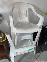 Stacked view of two white plastic chairs and one plastic stool beneath showing size and condition