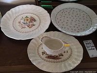 View of two Royal Doulton platters and one creamer with matching saucer on a wooden surface