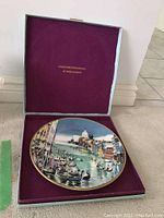 Photo showing the collectors plate inside original presentation box with purple lining, plate depicts the Grand Canal in Venice with gondolas and buildings.