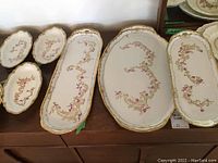 Photo of various vintage East Germany porcelain platters and dishes showing floral and gold decor, scalloped rims.