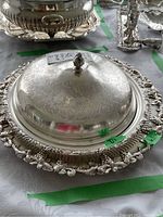 Inclined close-up of the silver plate tray with lid showing ornate designs and finial handle on the lid.