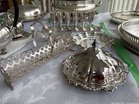 Silver plated covered butter dish, small silver plate dishes, and lattice-style serving caddy on white tablecloth