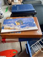 Top view of stacked collection items including a sealed polar bear cover coin and banknote set, brown Olympic stamp souvenir case, and several blue albums.