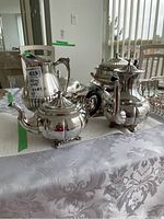 View of the full silver plated tea set including teapot, coffee pot, creamer, sugar bowl and water pitcher arranged on table