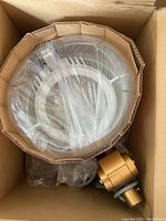 Top-down view of the vintage hard plastic hair dresser hood in original packaging, wrapped in plastic alongside gold-colored mounting clamp.