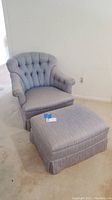 Light blue and gray striped upholstered arm chair with tufted back and rolled arms paired with rectangular matching ottoman with the same fabric and skirted base.