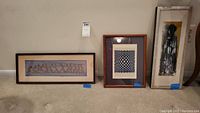 Three framed artworks displayed on a carpeted floor against a wall, showing overall condition and framing.