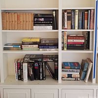 Wide view of multiple white shelves filled with hardcover books of various sizes and conditions.