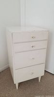 White wooden chest of drawers with four drawers closed, showing chipping on paint and small round knob handles