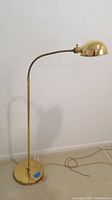 Full view of brass colored floor lamp with round base, slender vertical pole, and curved gooseneck with dome shade.