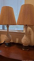 Full view showing both lamps with shades, placed on a wooden surface in front of window blinds.