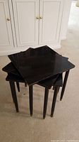 Photo showing the three black nesting tables stacked together, highlighting the size relative to each other and some wear on the legs.