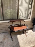 Side angled view showing the leather-like padded seat and backrest attached to a curved metal frame with rust on legs.