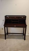 Front view of dark wood secretary desk showing three small drawers on top, vertical and horizontal compartments beneath them, and single pull-out drawer at the bottom.