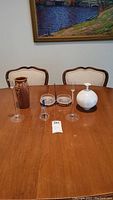 Full lot displayed on wooden table, showing all items including two vases (one ceramic, one white glass), two bowls with metal holder in center, two glass candle holders, and a glass bell.