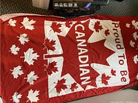 Large red and white Canadian towel with multiple maple leaves and 'Proud to Be Canadian' text laid flat on floor.