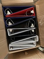 Box containing eight ring binders of various colors stacked vertically, showing metal ring mechanisms inside the binders.
